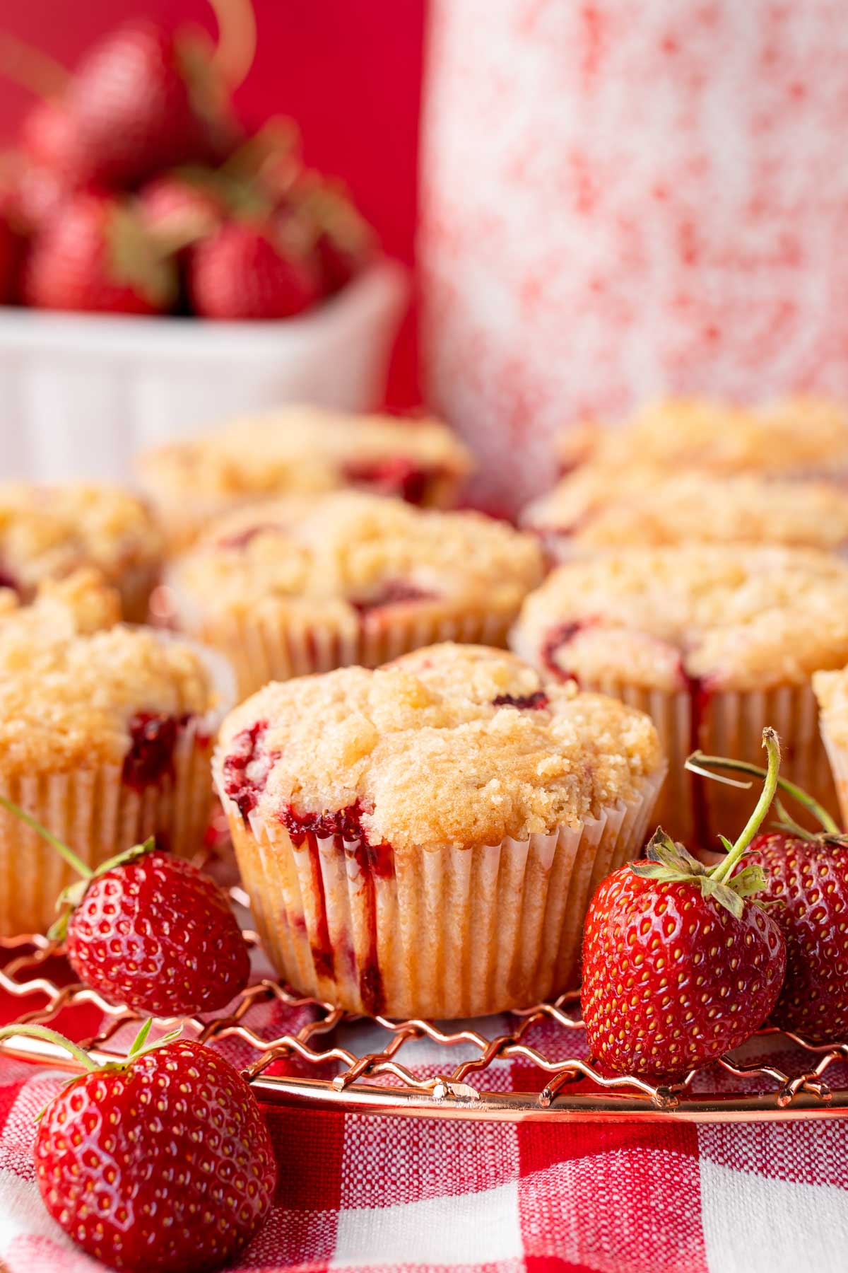 Strawberry muffins on a copper wire rack on a gingham napkin.