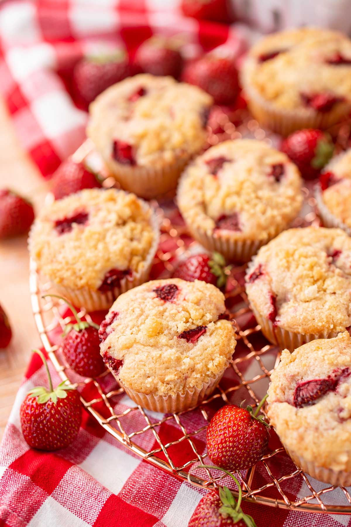 Strawberry muffins on a copper wire rack on a gingham napkin.