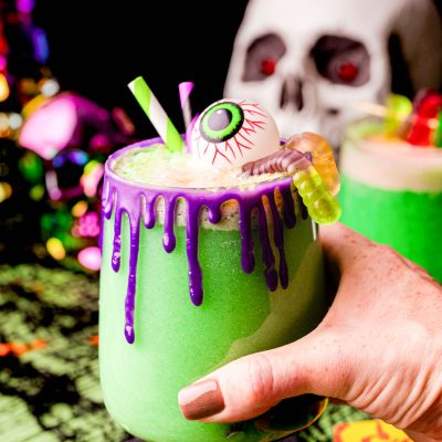 A woman's hand holding a cup of green Halloween party punch.