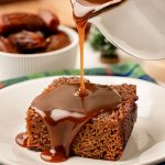 Toffee sauce being poured over the top of a slice of sticky toffee pudding.