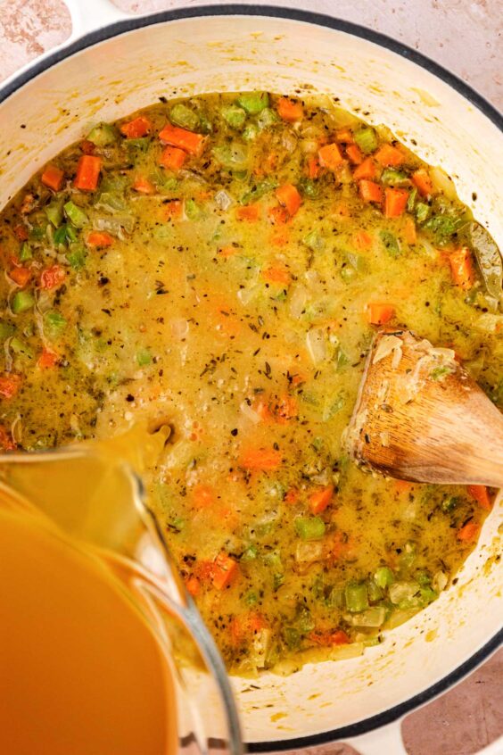 Broth being added to a pot of mise en place