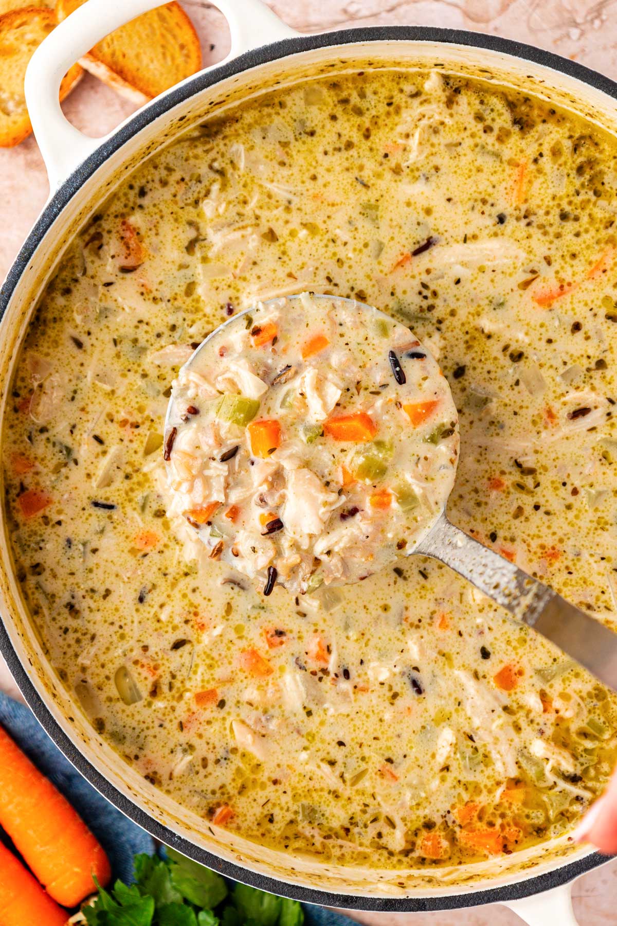 A ladle scooping wild rice and chicken soup out of a pot.