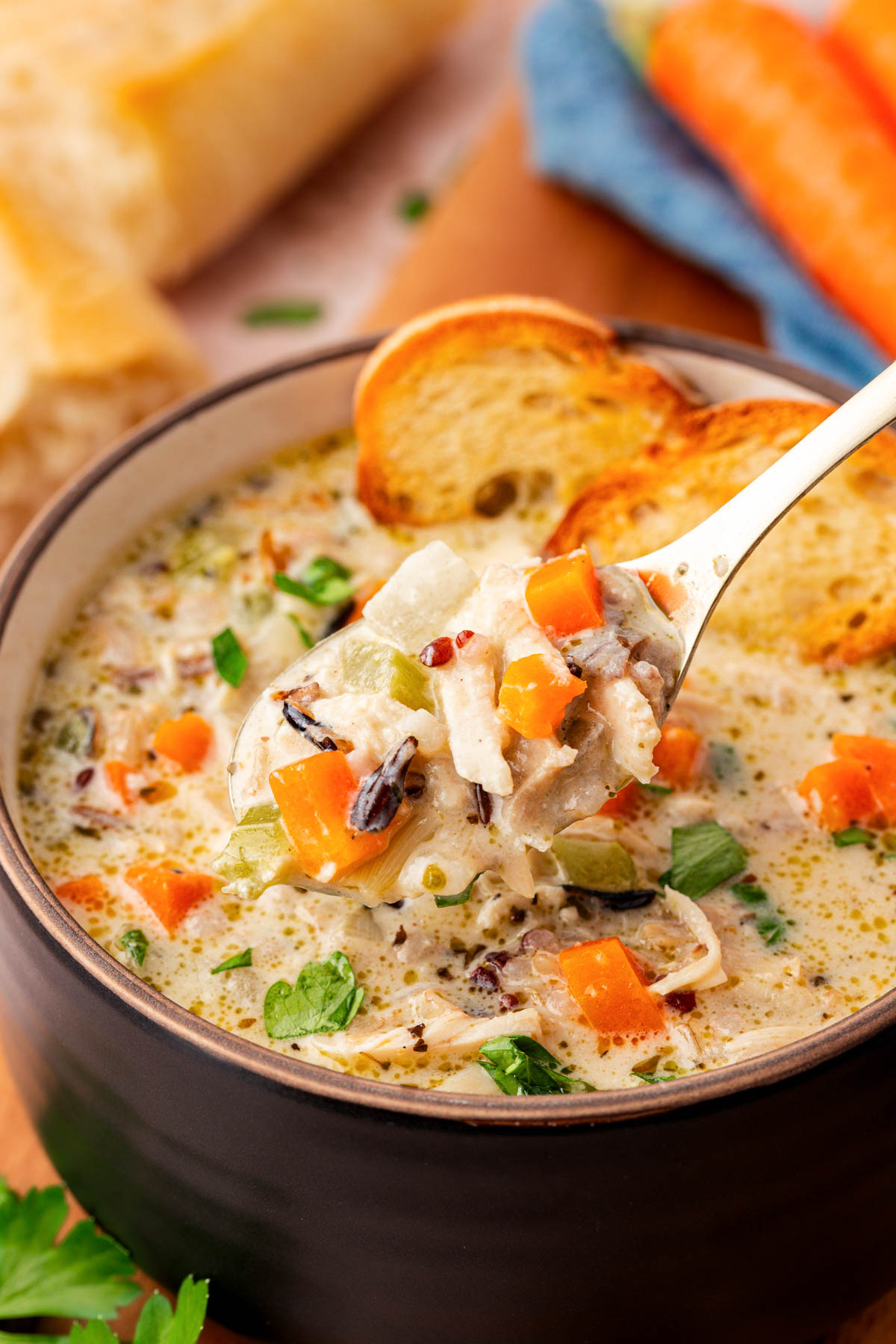 A spoonful of chicken and wild rice soup being lifted from a bowl.