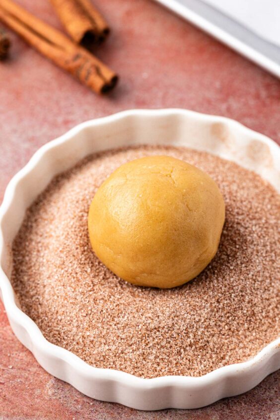 A ball of cookies dough being rolled in cinnamon sugar.