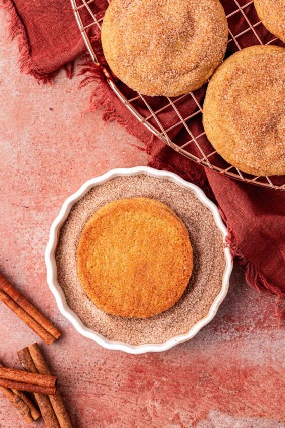 Close up of a snickerdoodle cookie being dipped in cinnamon sugar.