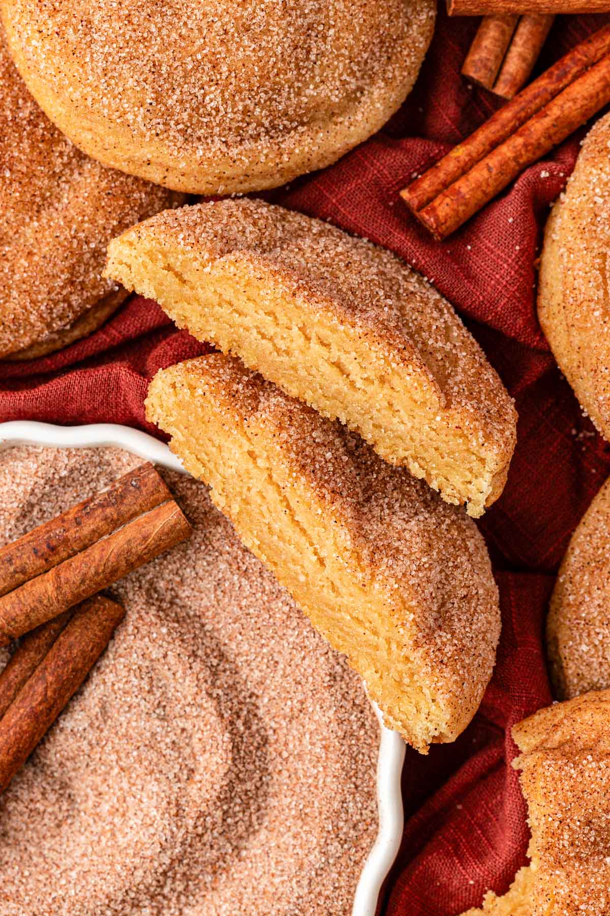 Large snickerdoodle cookies on a table, one has been cut in half to show the inner texture.