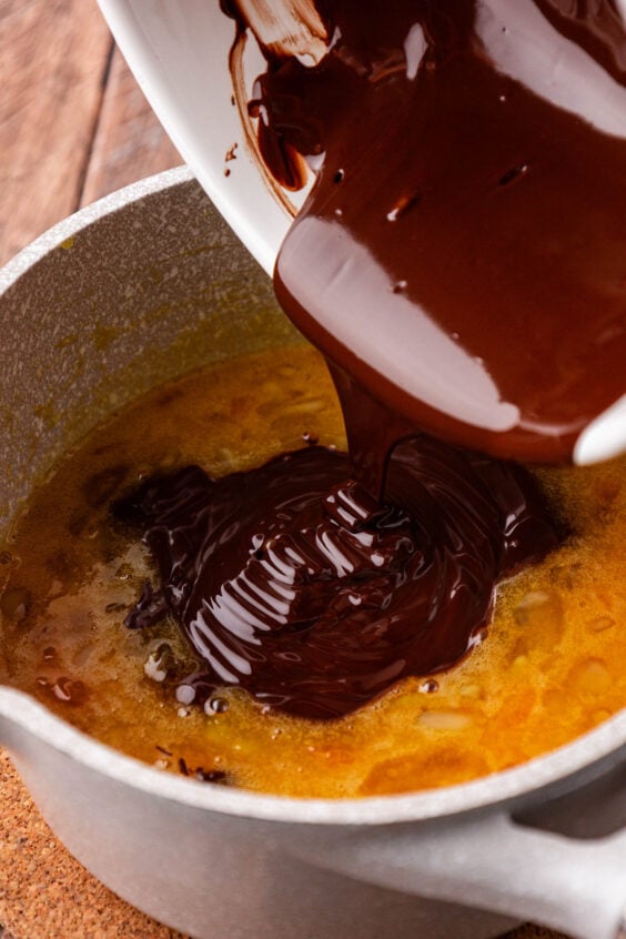 Melted chocolate being poured into a pot with eggs and sugar.