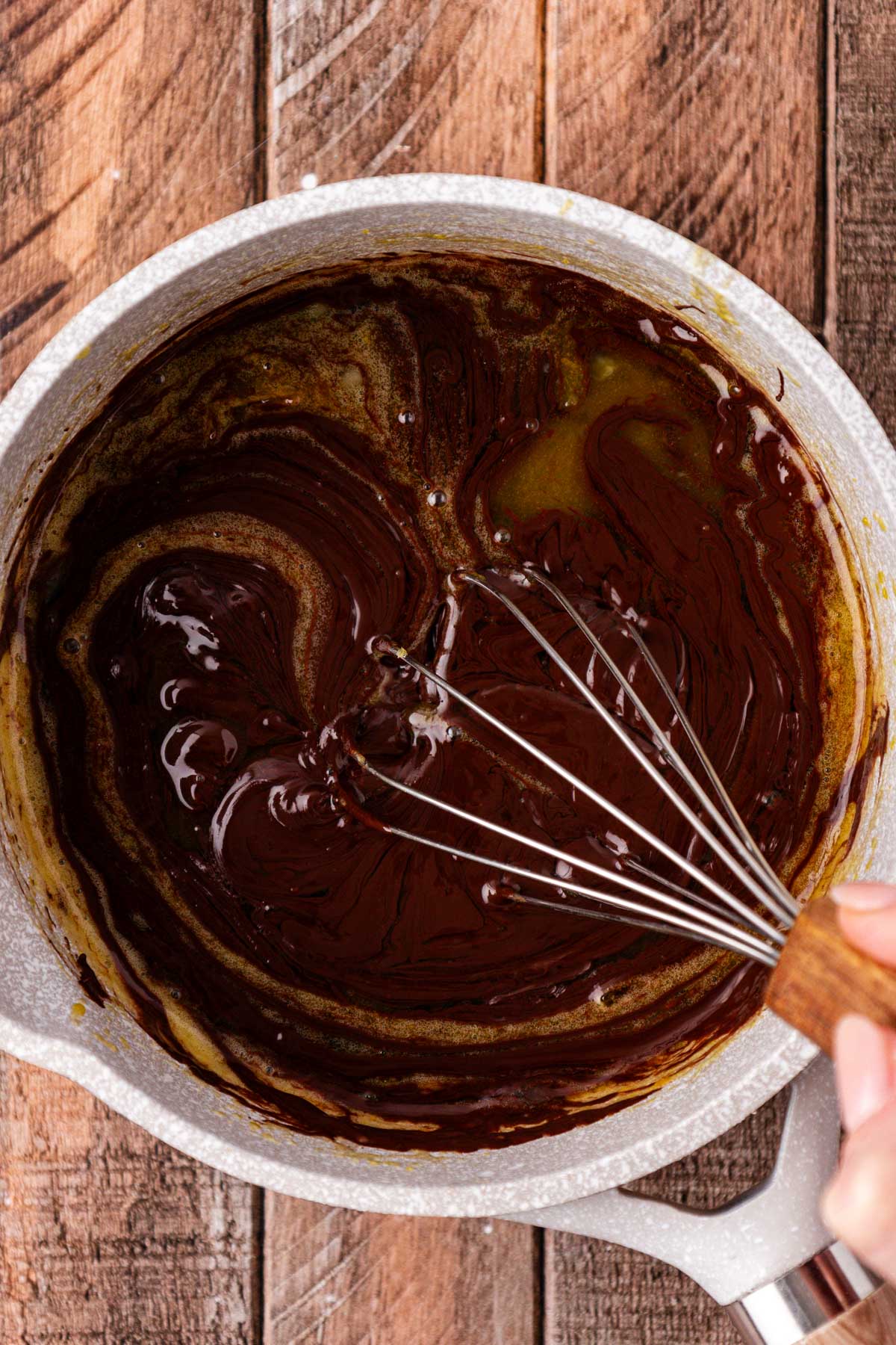 A whisk in a pot stirring chocolate and egg to make custard.