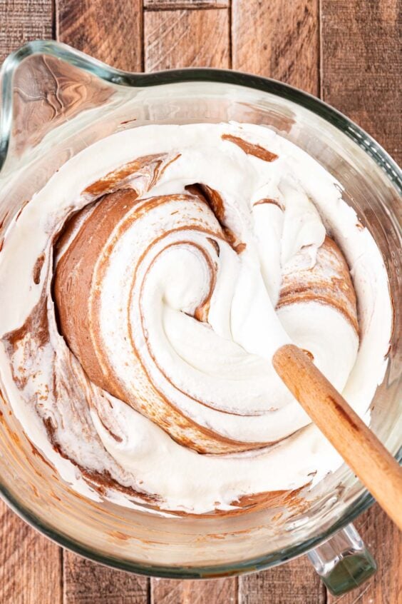 Whipped cream being poured into a chocolate pie mixture.