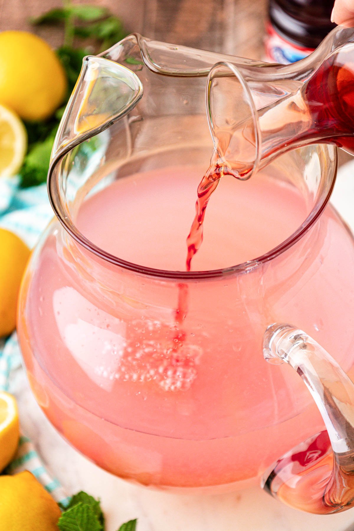 Cranberry juice being poured into a pitcher of lemonade.