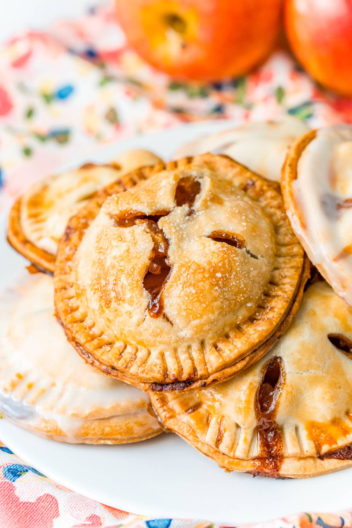 Apple hand pies on a white plate on a floral napkin with apples in the background.