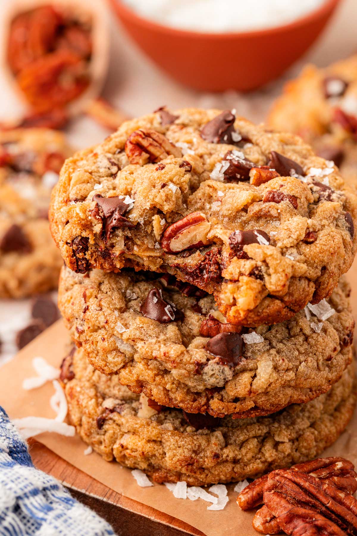 Close up of coconut pecan chocolate chip cookies stacked on a plate with the top one missing a bite.