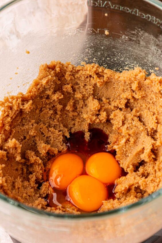 Vanilla and eggs being added to cookie dough in a mixing bowl.