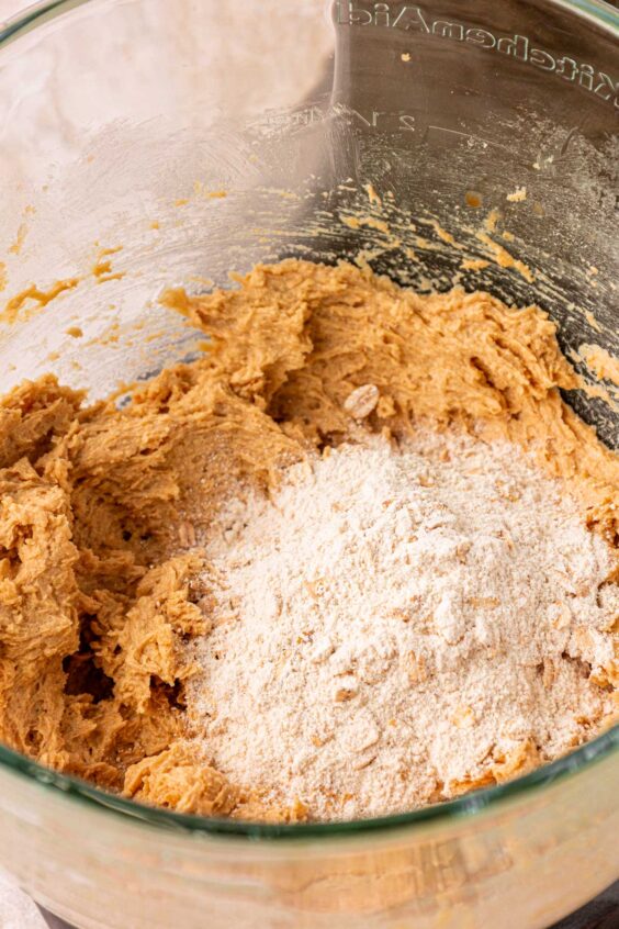 Dry ingredients being added to cookie dough in a mixing bowl.