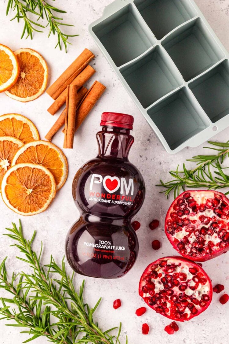 Overhead photo of a bottle of pomegranate juice and garnishes near an ice cube tray.