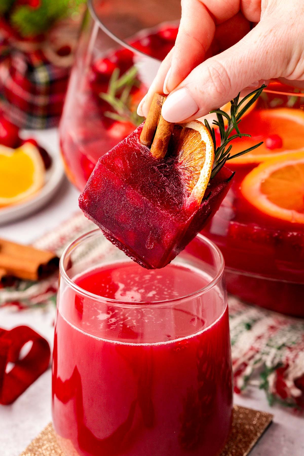 A festive pomegranate juice ice cube being dropped in a glass of Christmas punch.