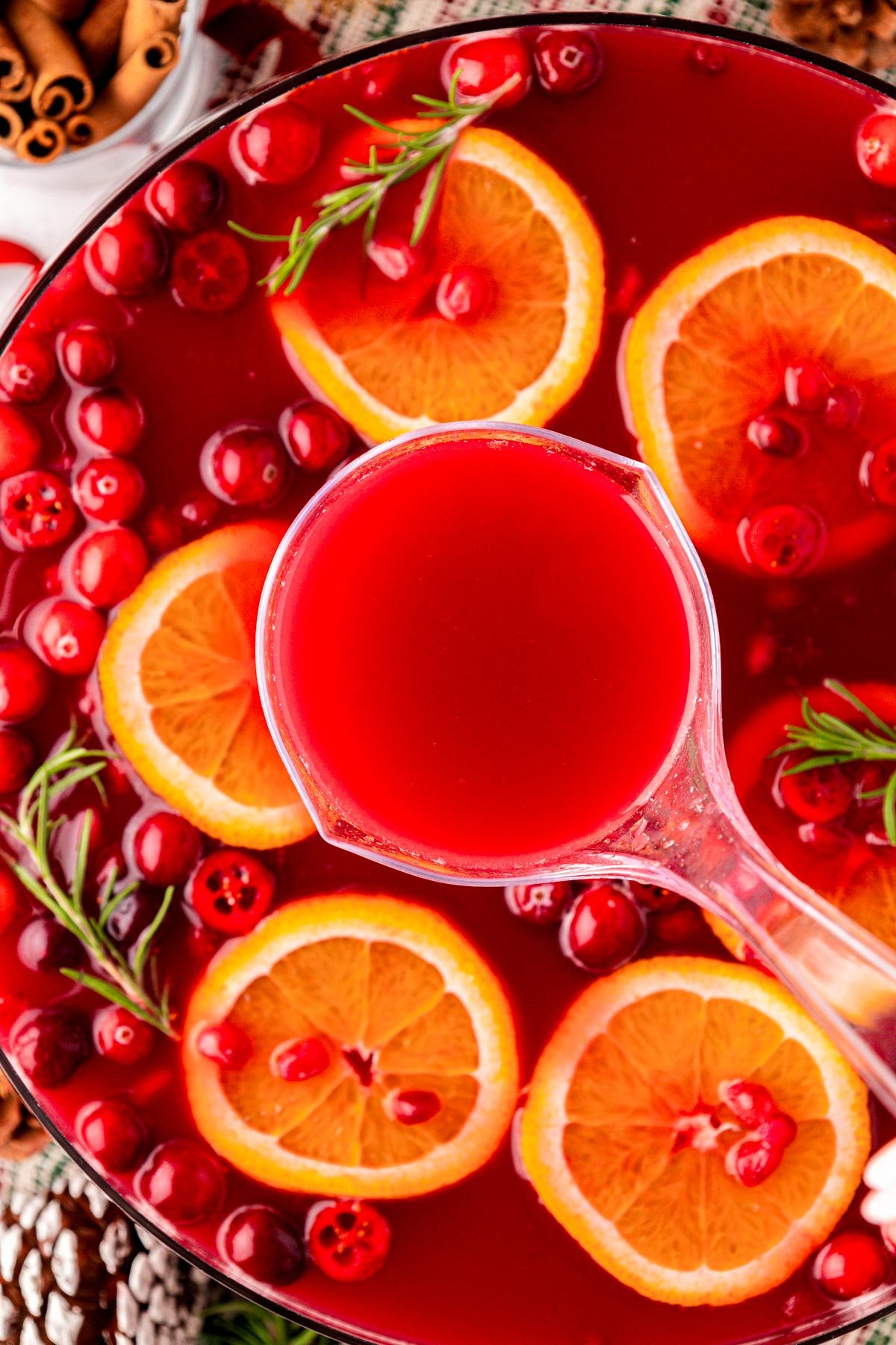 A ladle filled with red Christmas punch being lifted from a bowl of punch.