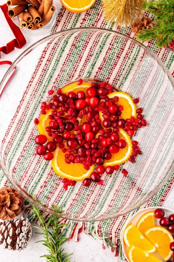 Sliced oranges, cranberries, and pomegranate arils in a punch bowl.