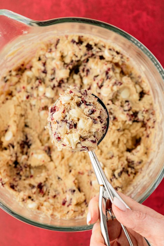 White chocolate cranberry cookie dough in a cookie scoop over a bowl of dough.