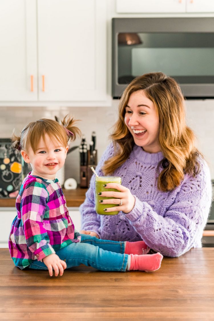 Toddler girl and her mother sharing a smoothie in the kitchen.