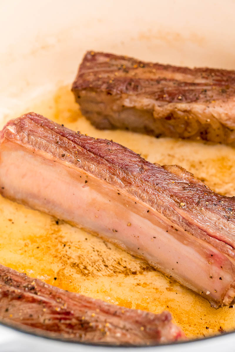 beef short ribs being seared in a dutch oven.