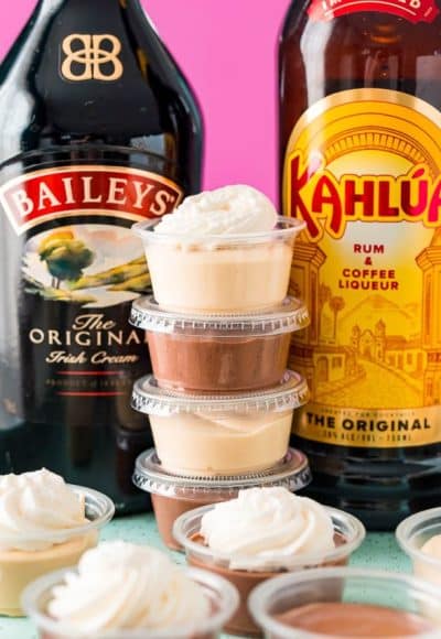 Stack of pudding shots between a bottle of Baileys and a bottle of Kahlua.