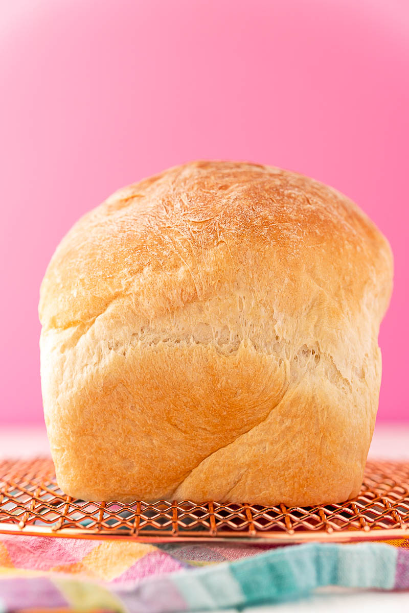 A loaf of white bread sitting on a cooling rack on to colorful napkin.