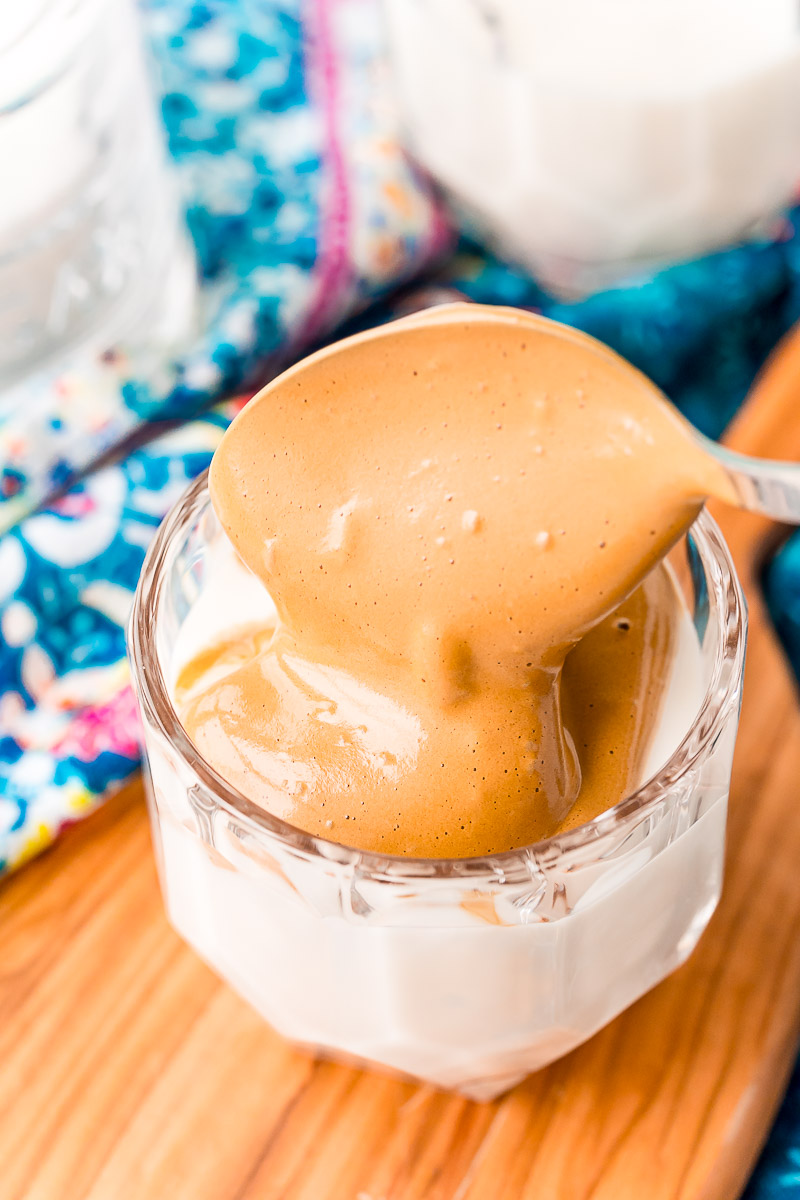 Whipped coffee being spooned over a glass of milk.