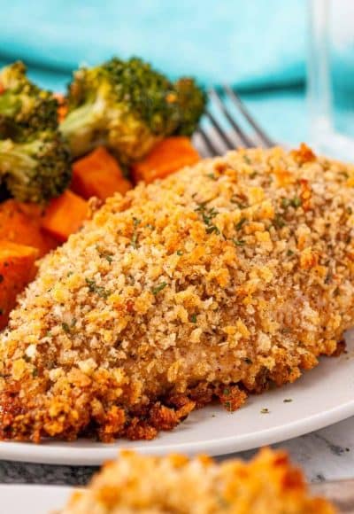 Breaded chicken breast on a white plate served with vegetables.