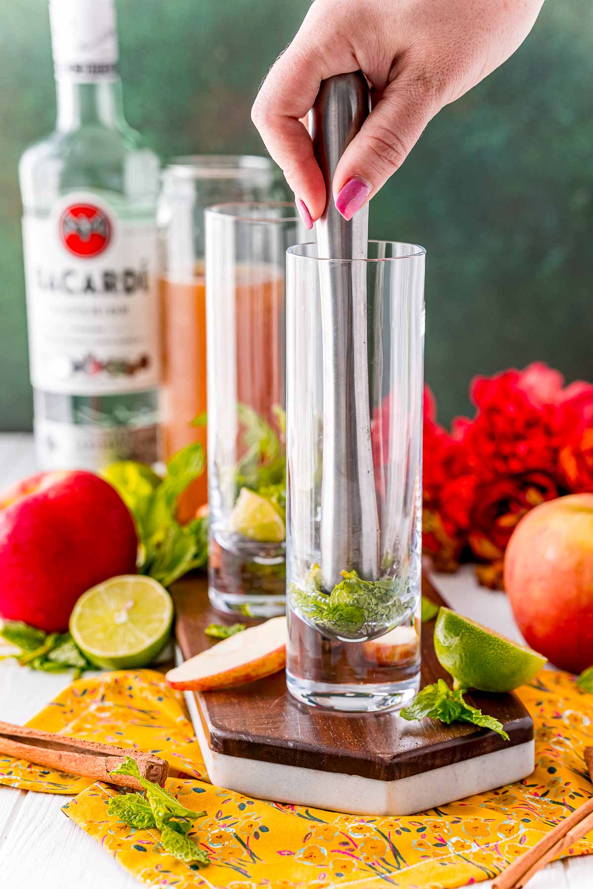 mint and limes being muddled in a tall glass.