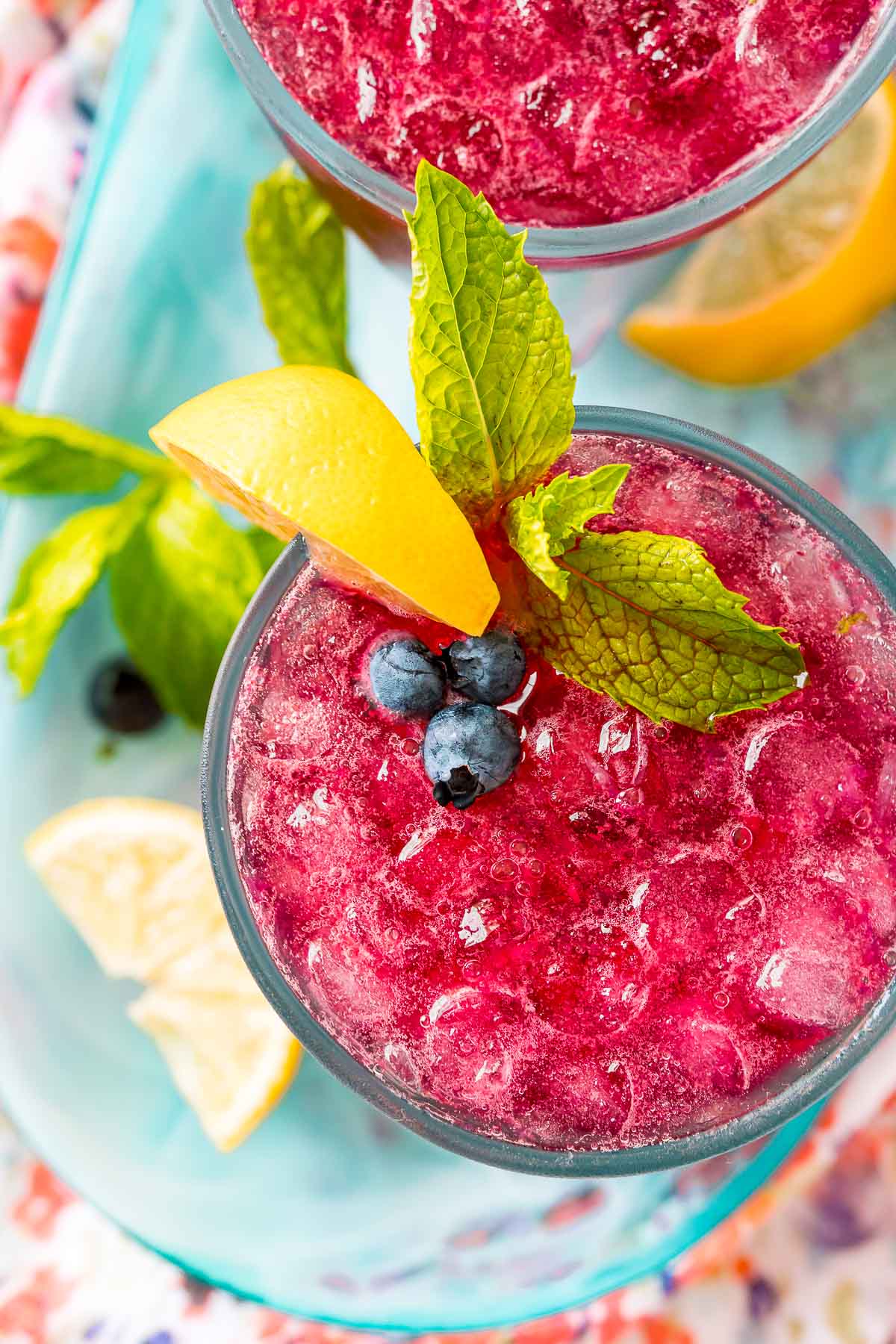 Overhead photo of a blueberry cocktail with lemon and mint garnish.