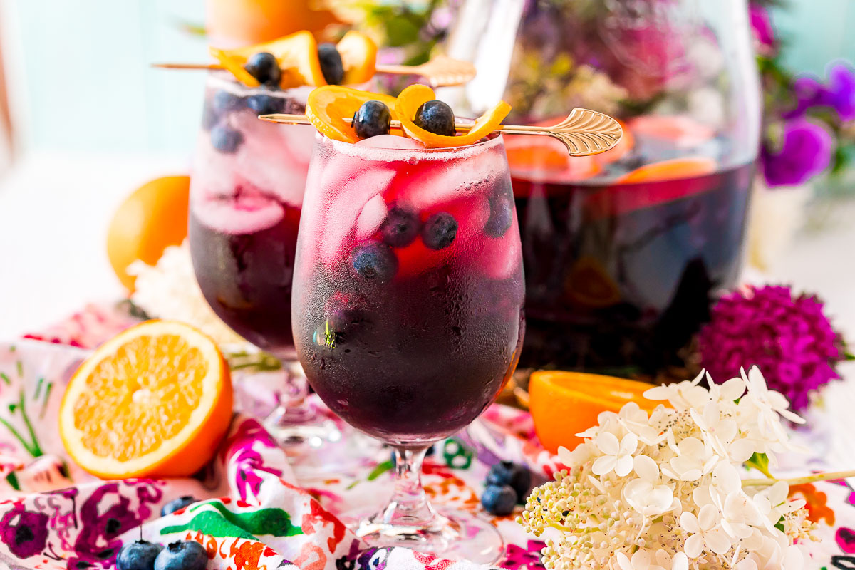 Photo of two wine glasses filled with blueberry sangria on a colorful floral napkin.