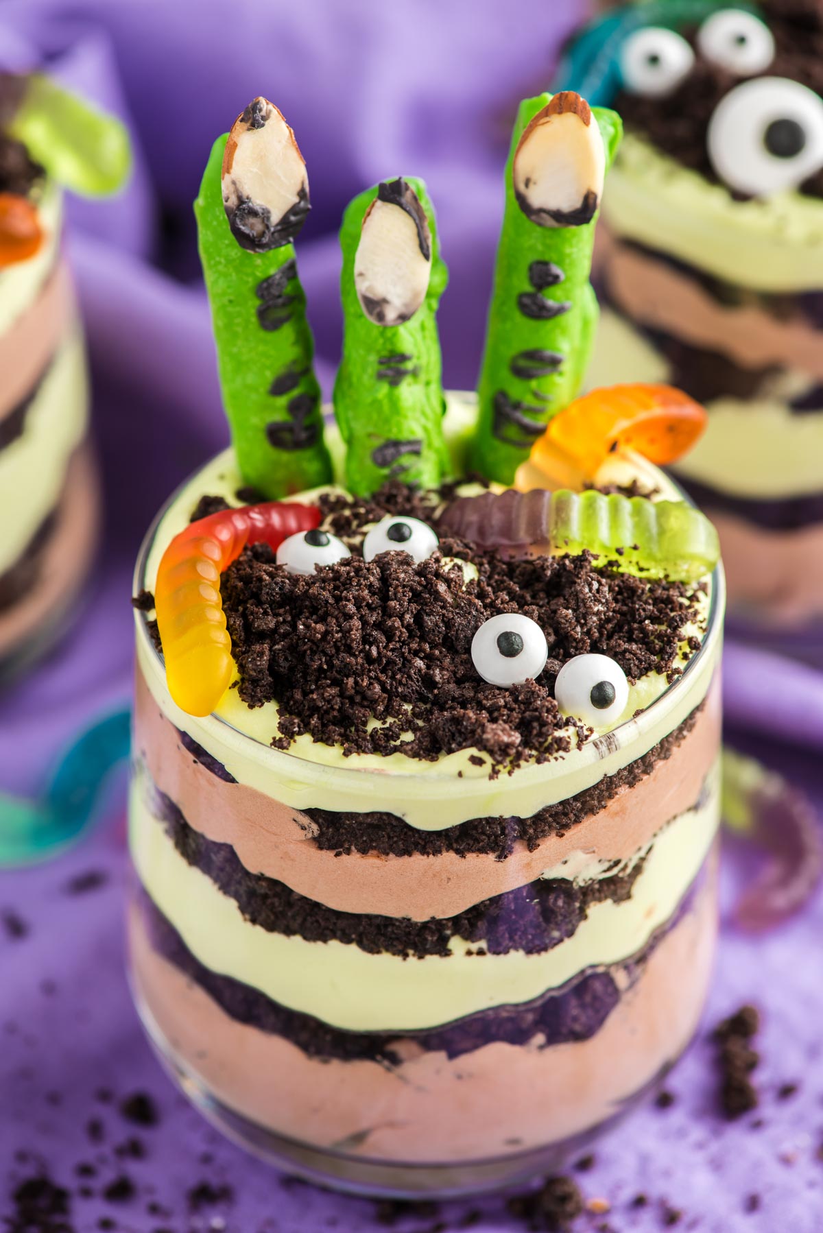 Close up photo of layers Halloween dirt cups with pretzel stick witch fingers, candy eyes, and gummy worms.