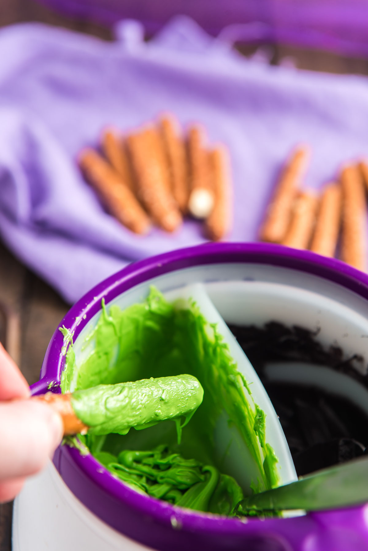 Pretzel rods being dipped in green candy melts.