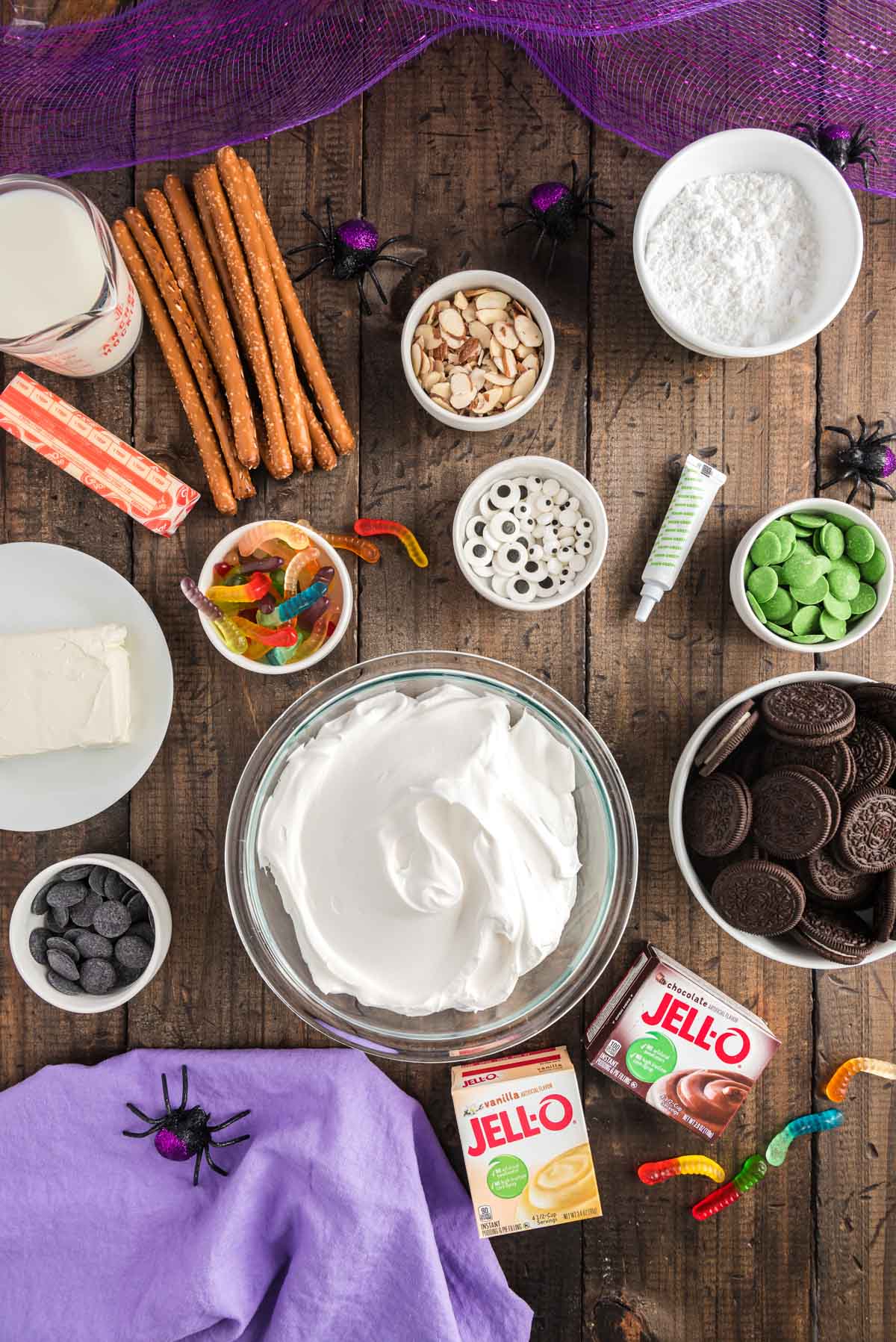 Overhead photo of ingredients to make Halloween themed dirt cups on a wooden table with a purple napkin.