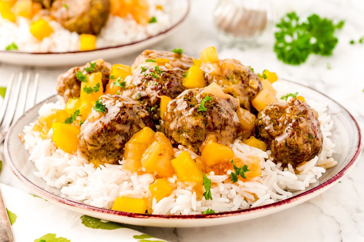 Close up photo of sweet and sour meatballs with pineapple on a plate of white rice.