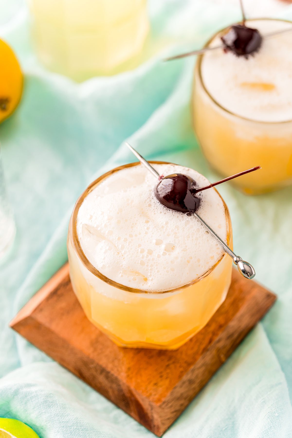 Whiskey sour in a cocktail glass on a wood coaster garnished with a cherry.