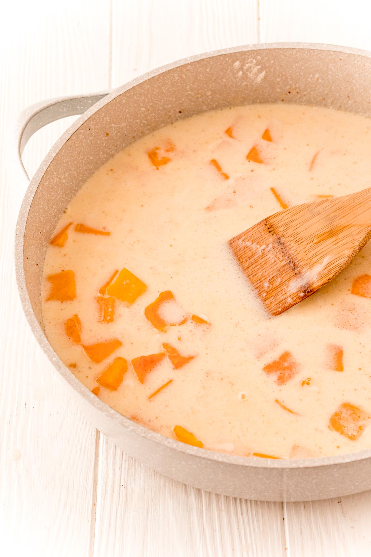 butternut squash cubes, broth, milk, and cream with spices cooking in a tan skillet.