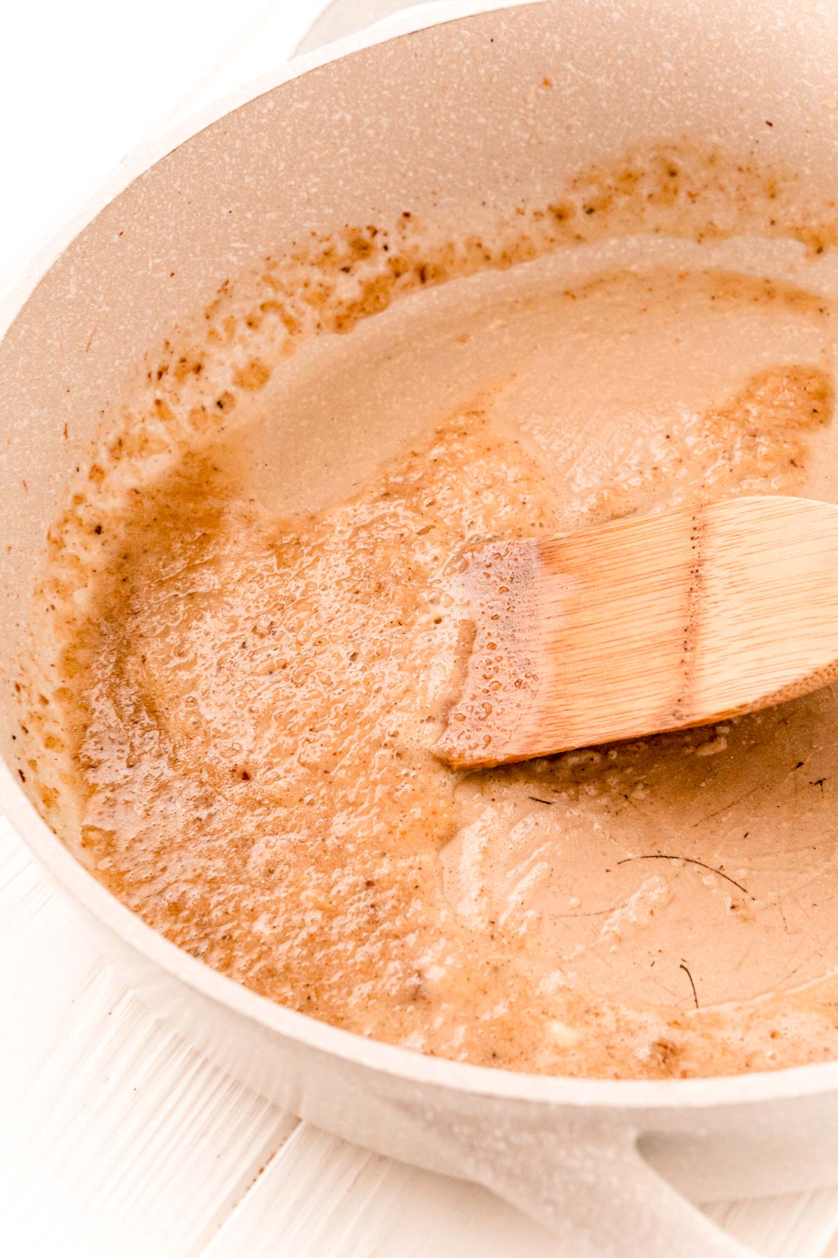 Garlic and flour being cooked in a tan skillet.