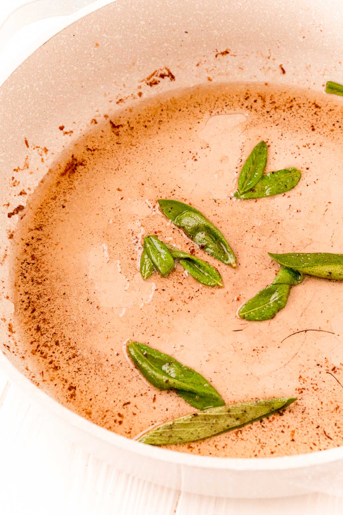 Sage being cooked in a tan frying pan.