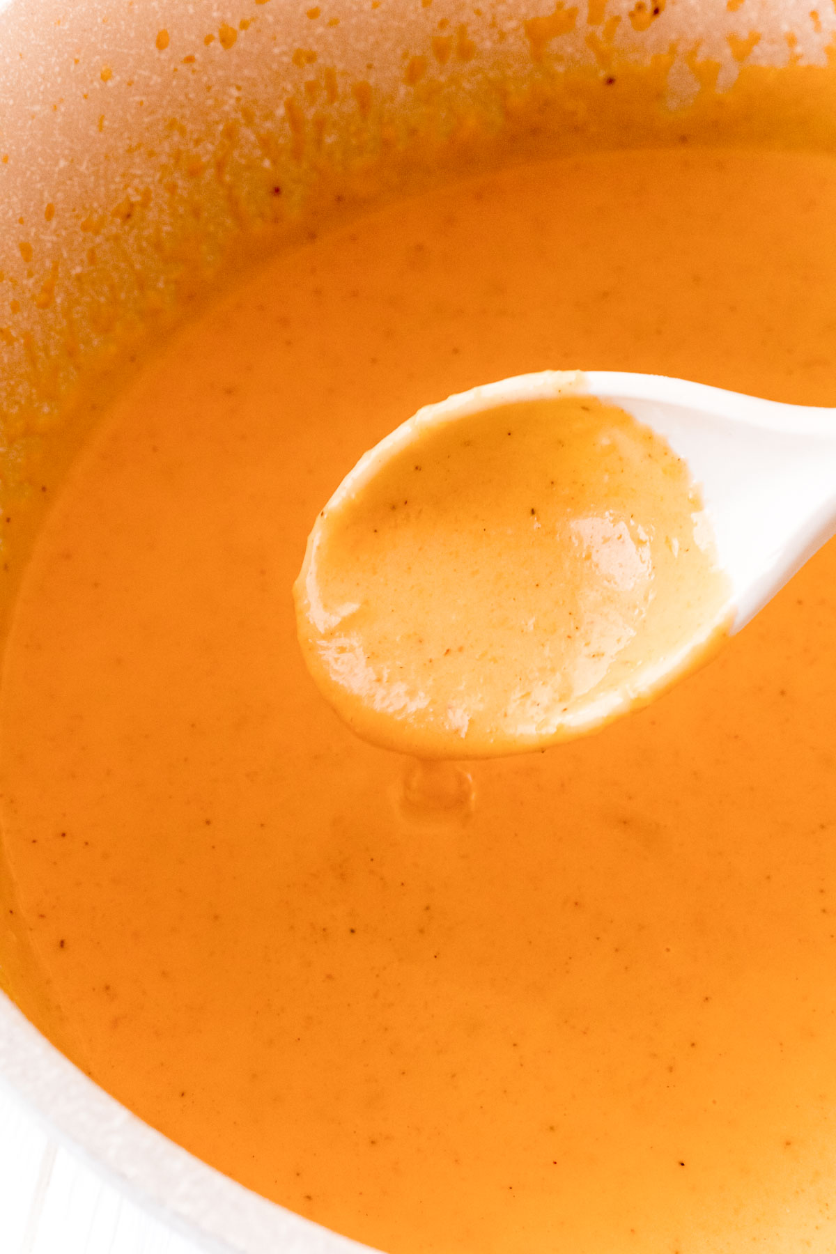 Butternut cream sauce in a pan being scooped up with a white spoon.