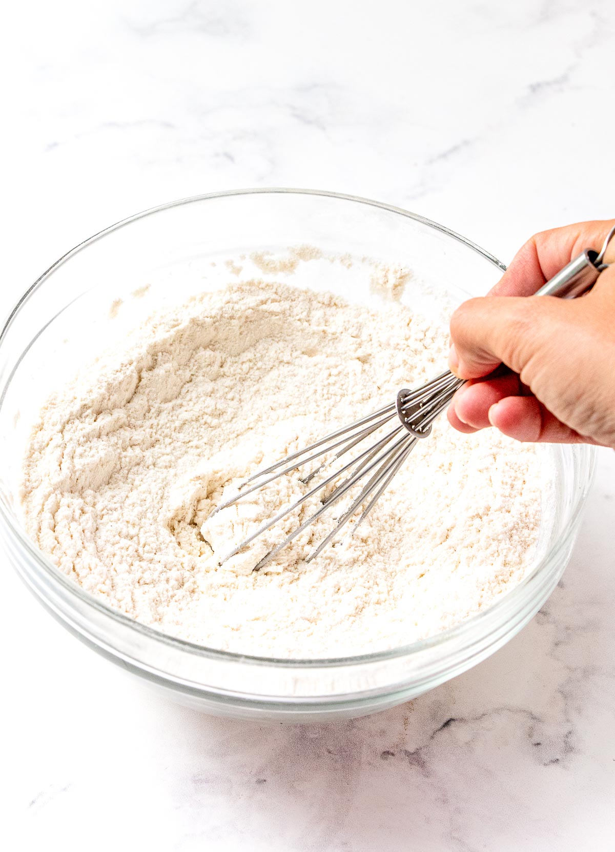 Dry ingredients for quick bread being whisked in a glass mixing bowl.