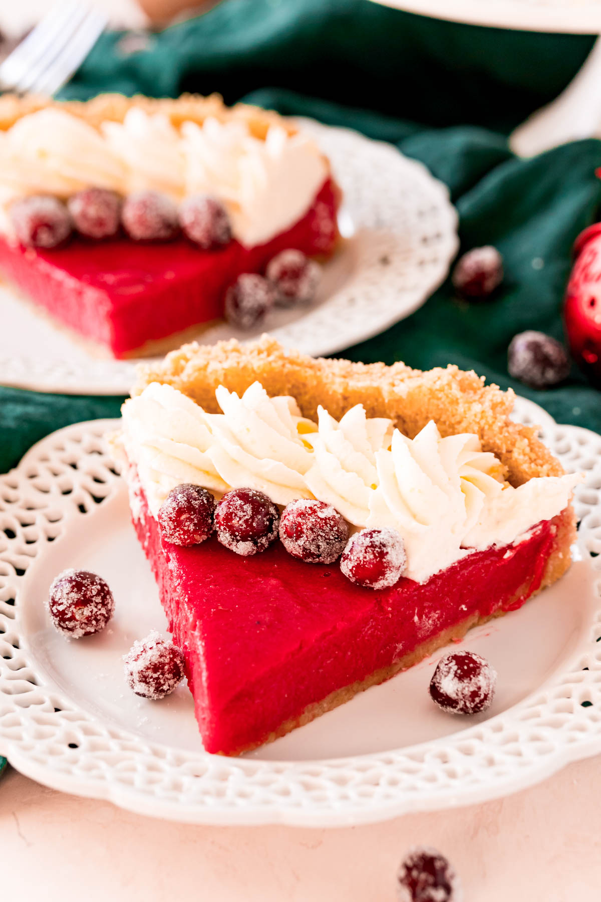 A slice of cranberry pie on a white plate topped with whipped cream and sugared cranberries.