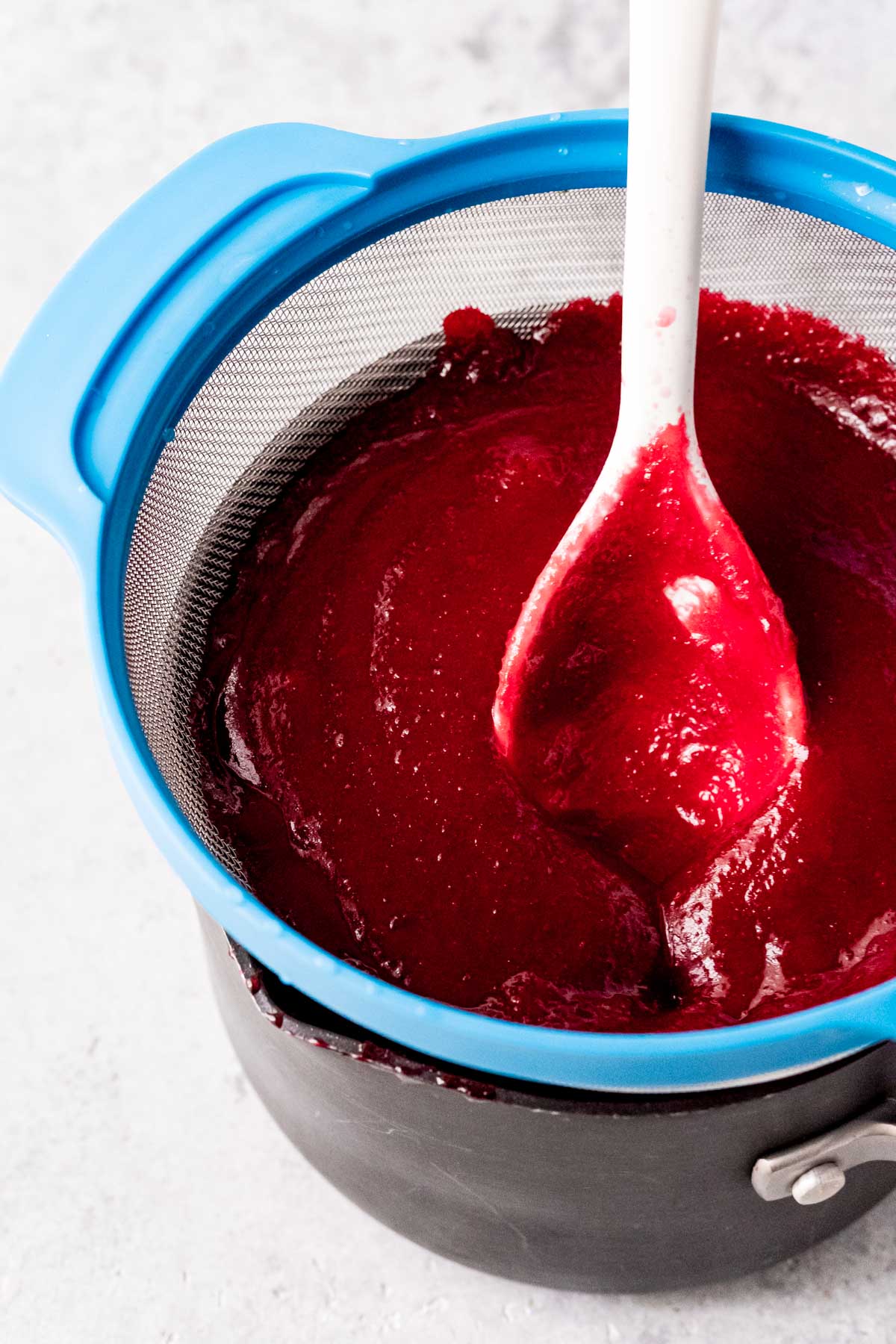 Cranberry mixture being pressed through a mesh strainer into a pan.