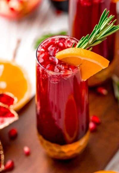 Close up photo of a pomegranate mimosa with orange and rosemary garnish.