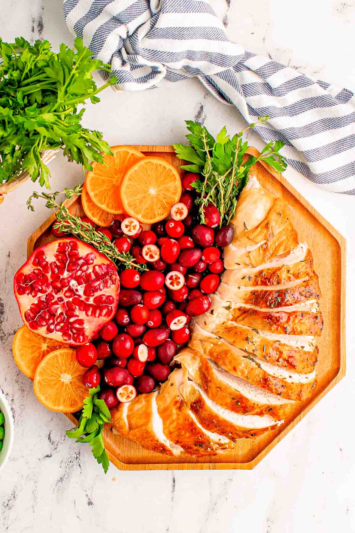 Overhead photo of sliced turkey bread on a wooden plate with cranberries, orange slices, pomegranate, and herbs for garnish.