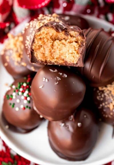 Close up photo of a stack of peanut butter balls on a white plate. The top one has a bite taken out of it.