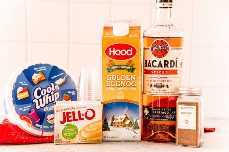 Ingredients to make pudding shots with eggnog and rum on a white table.