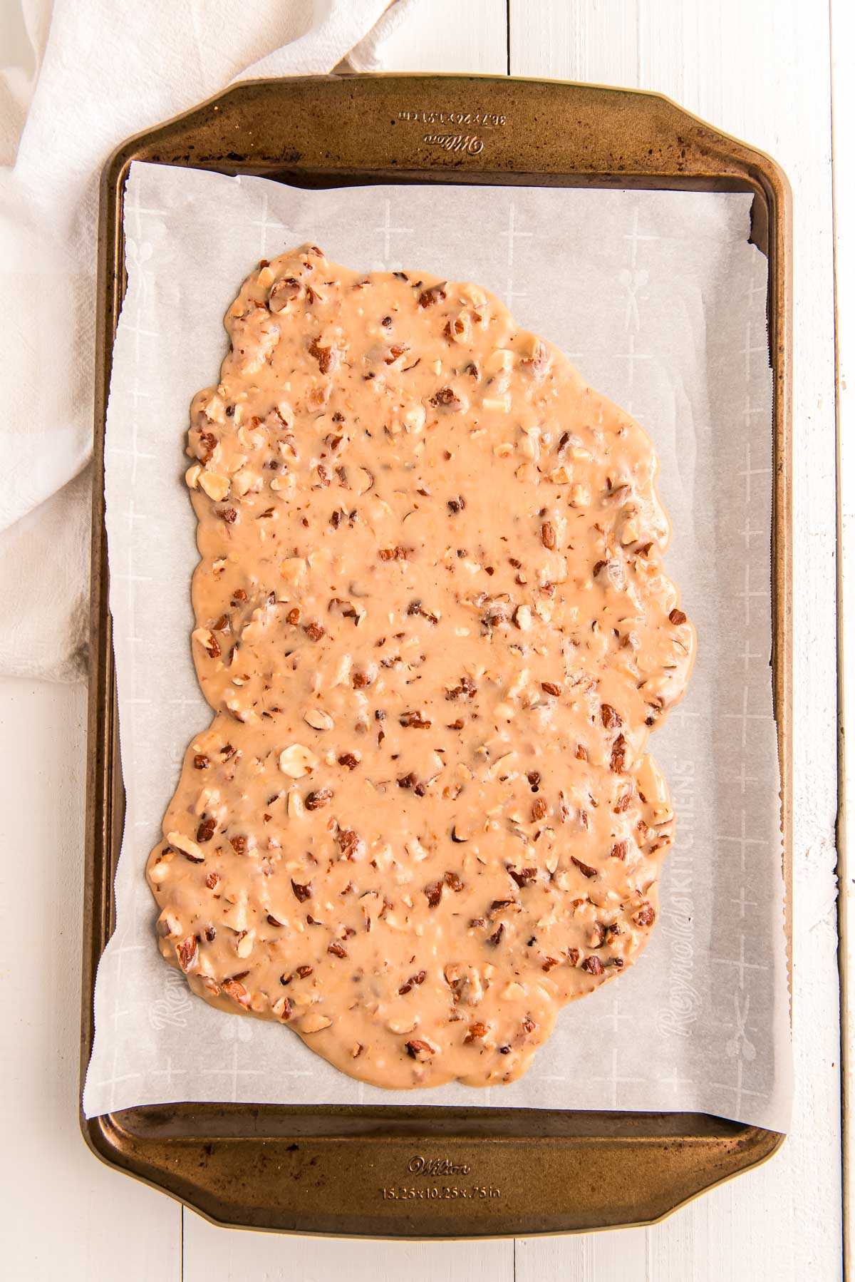 Overhead photo of a baking sheet with toffe spread out on parchment paper.