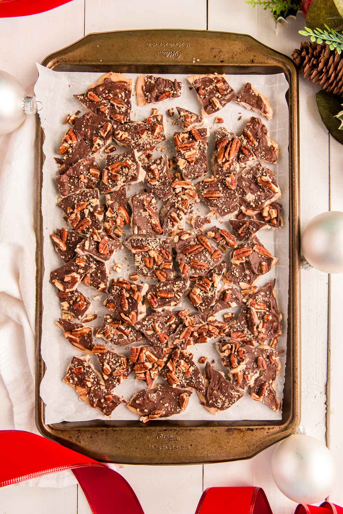 Overhead photo of cracked toffee on a baking sheet with holiday decorations around.